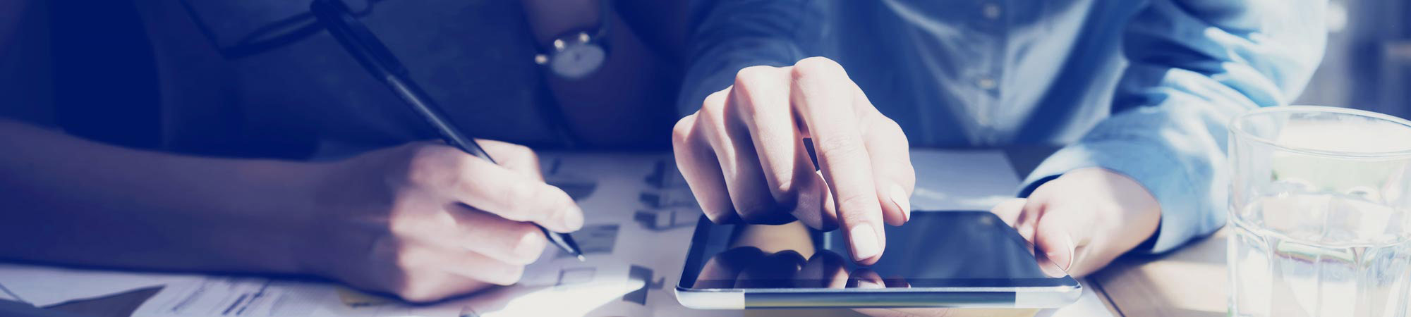 Tight shot of hands on tablet and another person taking notes
