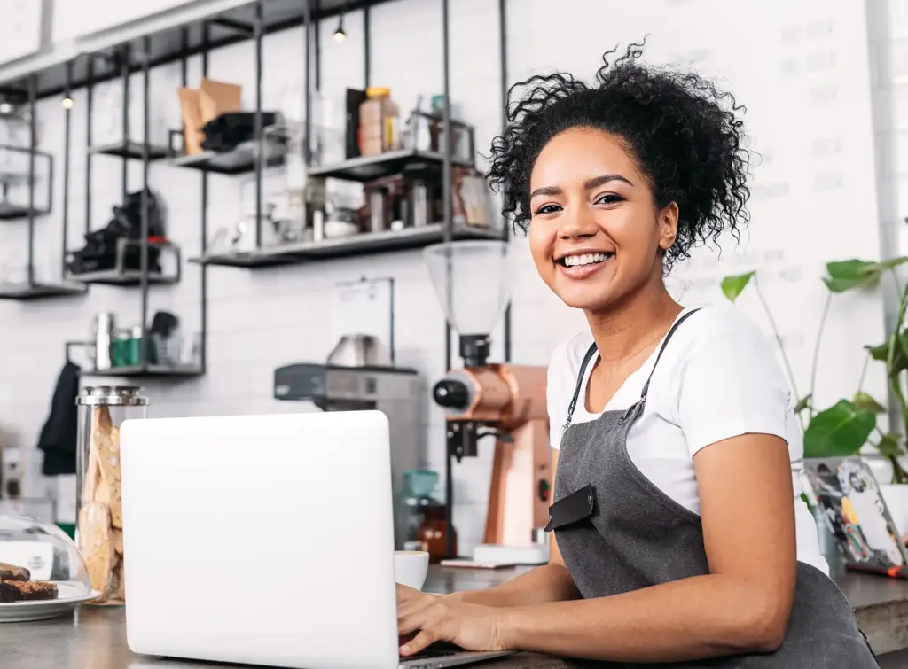 Woman in an apron with a laptop at the counter of cafe