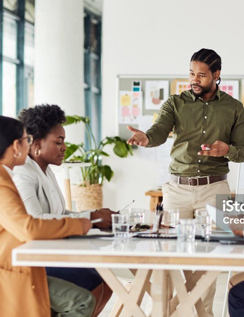 Man standing while addressing coworker at business meeting around table