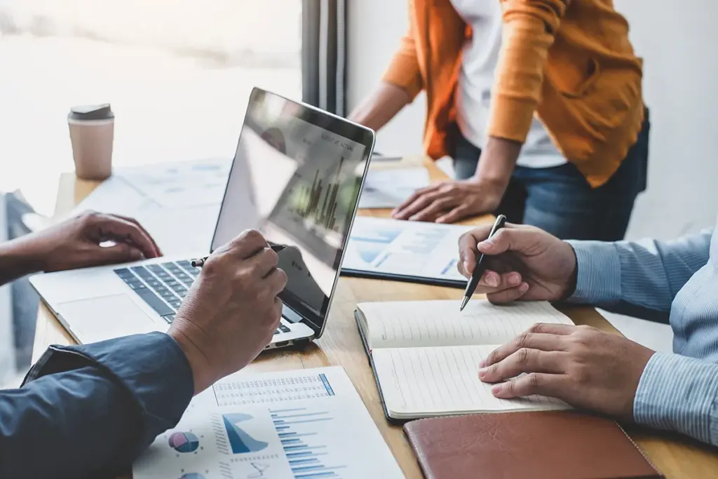 laptop open with graph showing results as team works at a table.