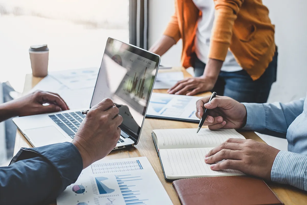 laptop open with graph showing results as team works at a table.