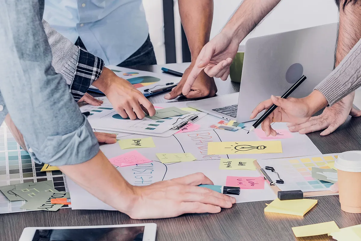 Post it and whiteboard on table with hands pointing during marketing meeting.