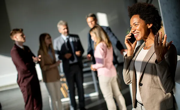 smiling businesswoman on phone with coworkers in background