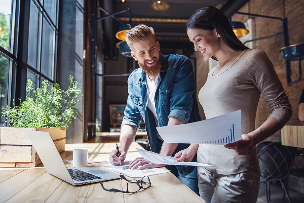 Man and woman surveying paperwork while working on laptop